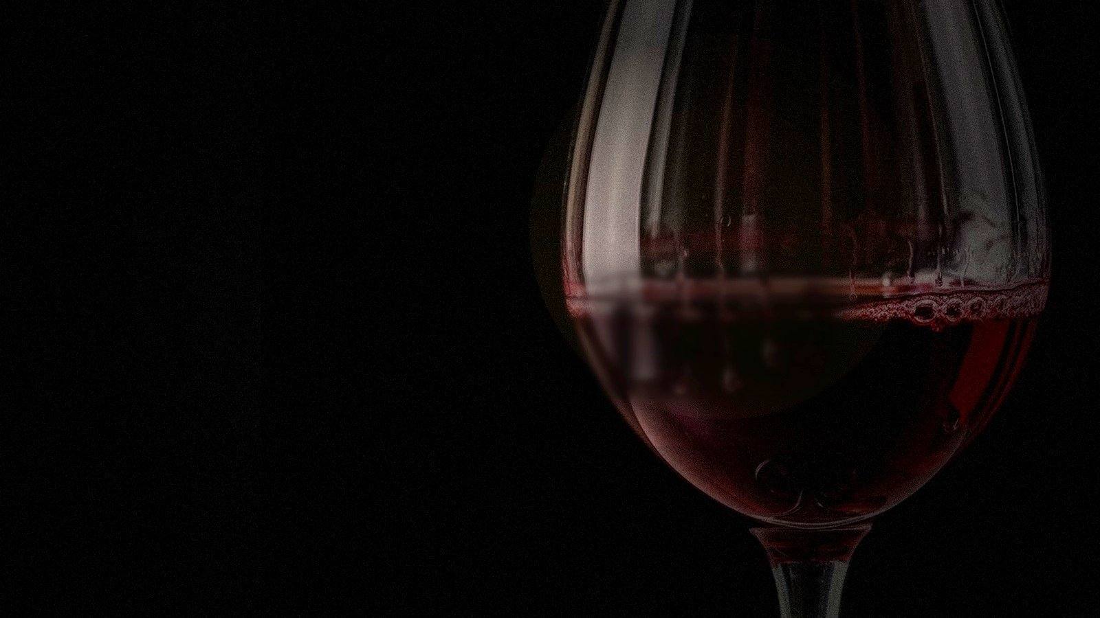 Una copa de vino tinto oscuro en sombra profunda, iluminada por un tenue borde de luz cálida.