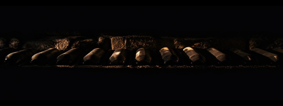Botellas tumbadas en un nicho de piedra, una sola luz rasante sobre los hombros.